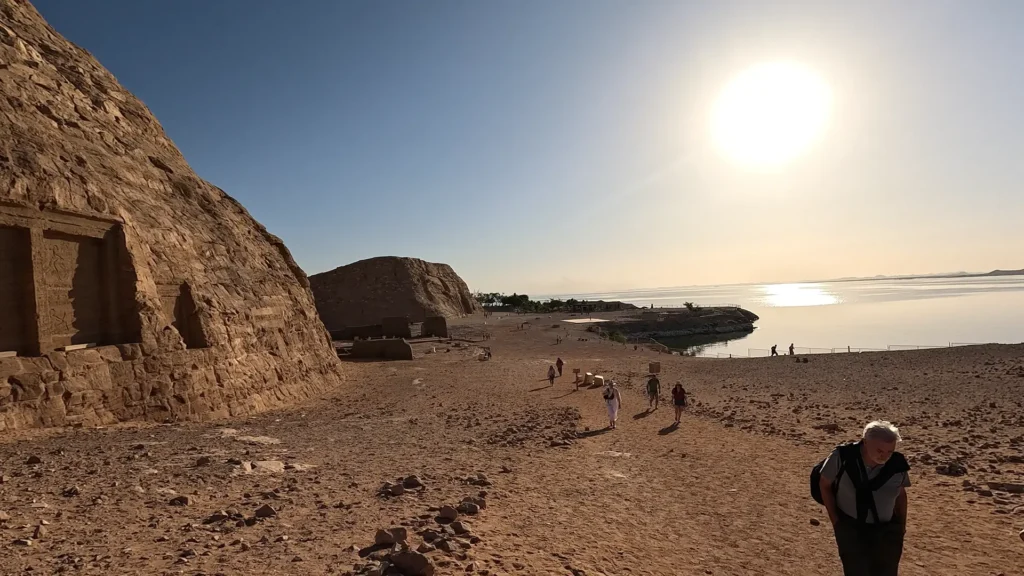 Turista caminhando sob sol forte no Egito, usando chapéu e carregando garrafa de água.
