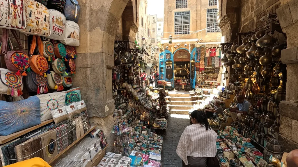 Mercado Khan el-Khalili no Cairo, com barracas coloridas e turistas comprando lembranças.